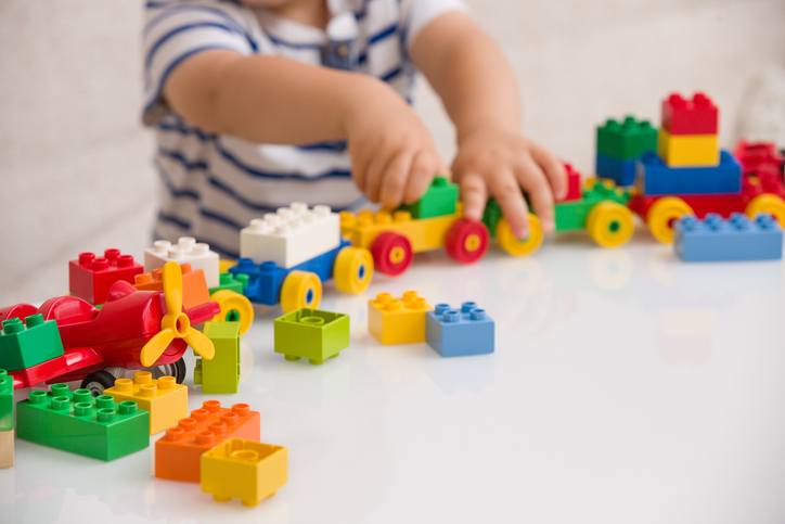 Close up of child's hands playing with colorful plastic bricks at the table. Toddler having fun and building out of bright constructor bricks. Early learning.  stripe background. Developing toys